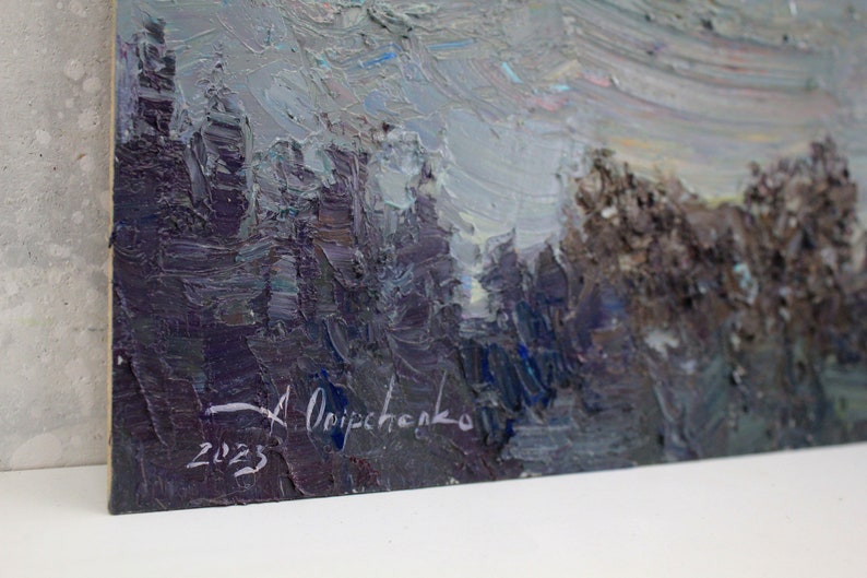 May include: Original oil painting on canvas. The artwork depicts a landscape with a forest and a cloudy sky. The color palette includes shades of gray, blue, and brown. Signed by the artist A. Onipchenko, with the year 2023.