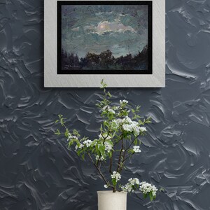 May include: An oil painting of a night landscape with a silver frame hangs on a textured gray wall. A vase with white flowers sits on a wooden table. The painting depicts a moonlit sky over a forest.