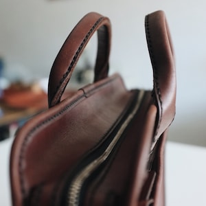 May include: A brown leather briefcase with a zipper closure and two handles. The briefcase has a stitched design and a textured surface.