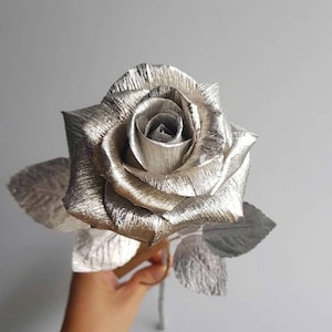 May include: A silver rose with metallic leaves. The rose is made of paper and has a realistic appearance.