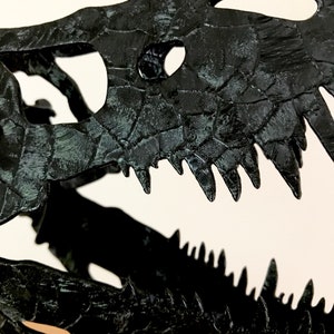 May include: Black dinosaur skull replica with detailed textured bone structure and sharp teeth.
