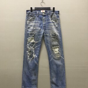 May include: Light blue denim jeans with distressed detailing, including rips and faded patches. The jeans are displayed on a hanger, showcasing the classic five-pocket design and button fly. The jeans have a worn, vintage aesthetic.