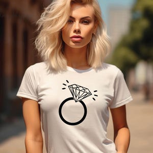 Pode incluir: Camiseta branca com um gr&aacute;fico preto de um anel de diamante. O anel &eacute; estilizado com um design simples e tem um &uacute;nico diamante.