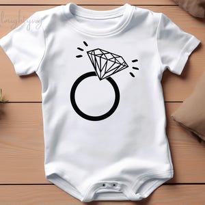 Pode incluir: Macac&atilde;o branco para beb&ecirc; com um gr&aacute;fico de anel e diamante preto.
