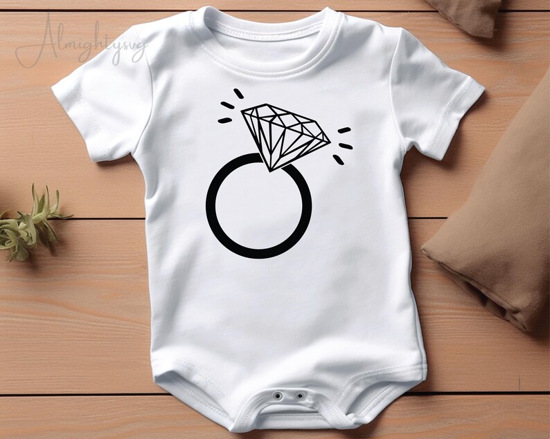 Pode incluir: Macac&atilde;o branco para beb&ecirc; com um gr&aacute;fico de anel e diamante preto.