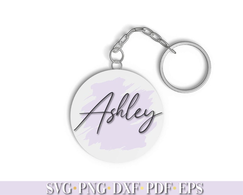 May include: A white circle keychain with a light purple watercolor background and the name "Ashley" written in black cursive.