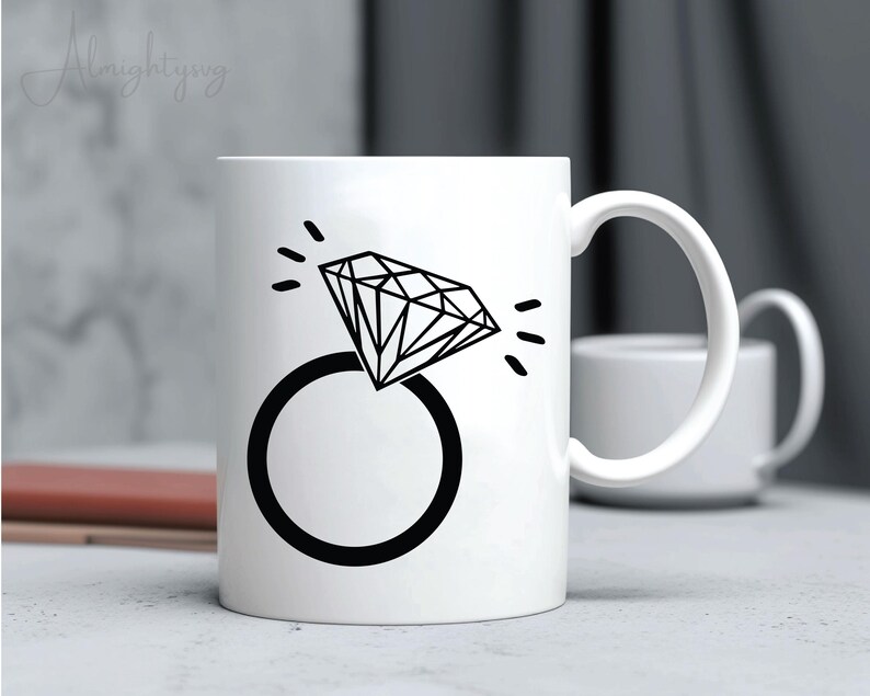 Pode incluir: Caneca de cer&acirc;mica branca com um gr&aacute;fico preto de um anel de diamante. O anel &eacute; estilizado com um design simples e o diamante &eacute; delineado com linhas pretas.