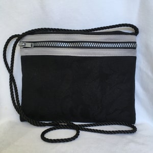 Bolsa de viaje, bolsa para pasaporte en color negro con ribete de tela gris, para llevar cruzada o al hombro.