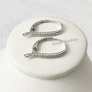 May include: A pair of silver earring findings with a row of small clear stones around the edge of each hoop.