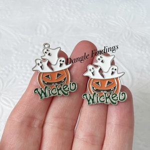 Pode incluir: Dois pingentes de prata com uma ab&oacute;bora e fantasmas. As ab&oacute;boras s&atilde;o laranja com um caule verde e uma cara esculpida. Os fantasmas s&atilde;o brancos com olhos e bocas pretos. A palavra "Wicked" est&aacute; escrita em letras verdes em cada pingente.