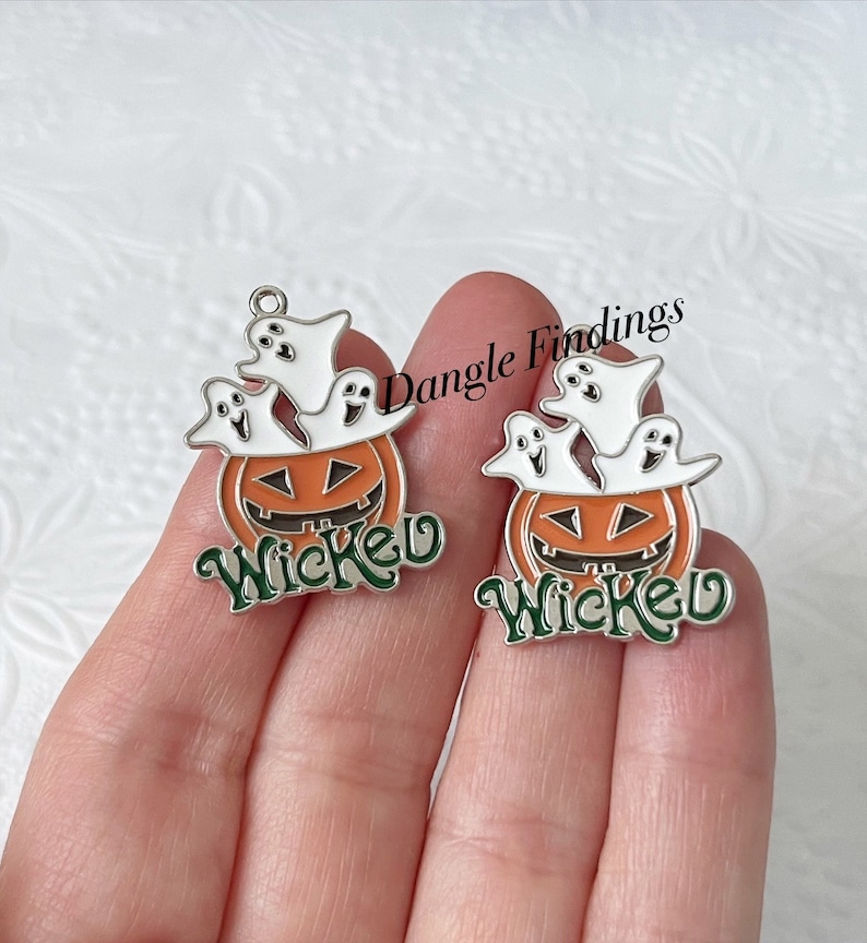 Pode incluir: Dois pingentes de prata com uma ab&oacute;bora e fantasmas. As ab&oacute;boras s&atilde;o laranja com um caule verde e uma cara esculpida. Os fantasmas s&atilde;o brancos com olhos e bocas pretos. A palavra "Wicked" est&aacute; escrita em letras verdes em cada pingente.