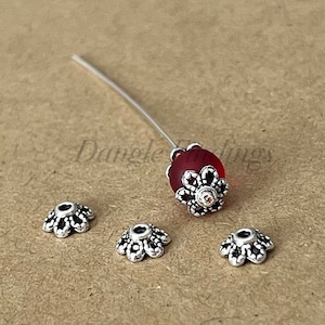 May include: Four silver-toned bead caps with a scalloped edge and a red glass bead with a silver-toned cap.