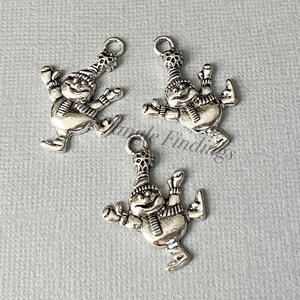 May include: Three silver charm pendants featuring a snowman ice skating. Each charm has a loop for attaching to a necklace or bracelet.