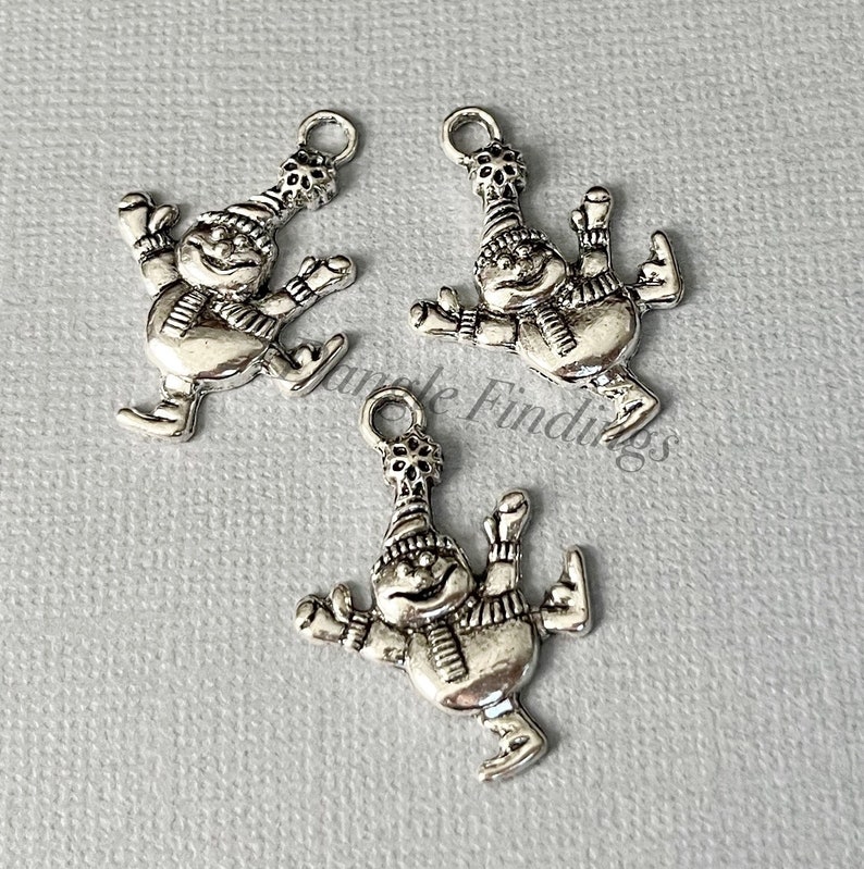 May include: Three silver charm pendants featuring a snowman ice skating. Each charm has a loop for attaching to a necklace or bracelet.