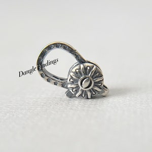 May include: A silver-toned clasp with a floral design and a loop adorned with star-shaped cutouts. The clasp features the text "Dangle Findings". The floral design has a central circular element surrounded by petal-like shapes.