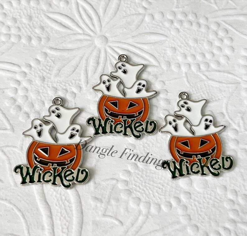 Pode incluir: Tr&ecirc;s pingentes de prata com um design de ab&oacute;bora com cara de jack-o'-lantern e tr&ecirc;s fantasmas dentro. A ab&oacute;bora &eacute; laranja com um caule verde e a palavra "Wicked" escrita em letras verdes abaixo da ab&oacute;bora.