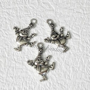 May include: Three silver charm pendants featuring a snowman ice skating. Each charm has a loop for attaching to a necklace or bracelet.