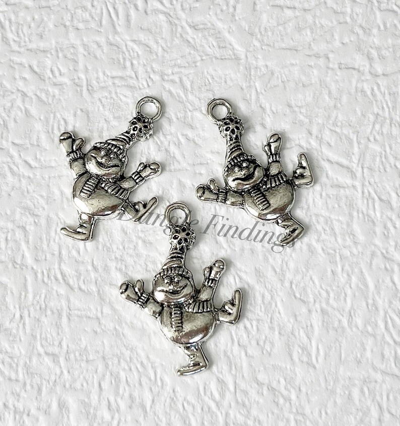 May include: Three silver charm pendants featuring a snowman ice skating. Each charm has a loop for attaching to a necklace or bracelet.
