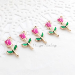 May include: Six gold-tone rose charms with pink roses and green leaves. Dangle Findings is printed on the white surface.
