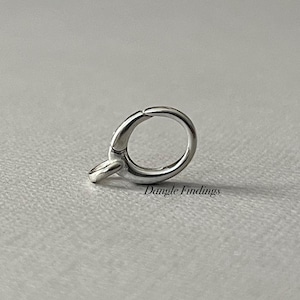 May include: A silver-colored jewelry clasp with a circular ring and a small, rectangular attachment. The clasp is designed to connect two pieces of jewelry. The text "Dangle Findings" is printed on the surface.