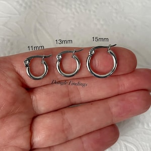 May include: Three silver hoop earrings with a small clear stone on the hinge. The hoops are 11mm, 13mm, and 15mm in diameter. Dangle Findings is written below the hoops.