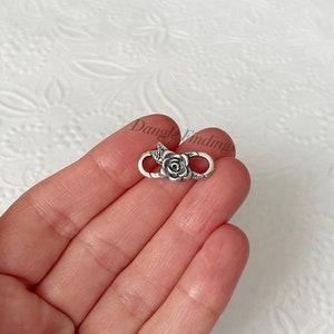 May include: Silver-toned rose flower charm with a loop on each side. The charm is designed to be used as a connector for jewelry making.