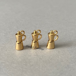 May include: Three gold-colored metal charms shaped like coffee pots. Each charm has a loop at the top for attaching to a necklace or bracelet.