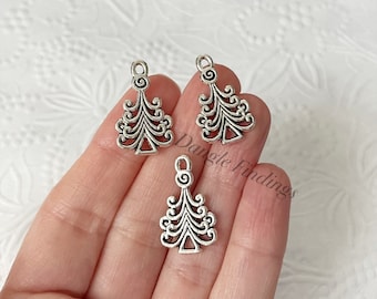 May include: Three silver-toned Christmas tree charms with intricate designs. The charms are about 1 inch tall and have a loop at the top for hanging.