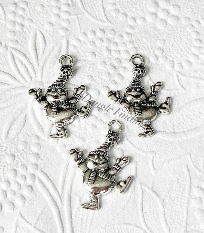 May include: Three silver charm pendants of a snowman ice skating. Each charm has a loop at the top for attaching to a necklace or bracelet.