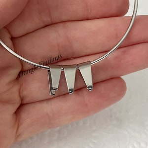 May include: Close-up of a silver-colored necklace with three triangular pendant findings. The text "Dangle Findings" is visible on the left side of the image. The necklace is on a white background.