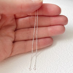 May include: A pair of silver chain earrings with a simple design. The earrings are long and dangle from the earlobe.