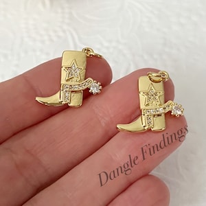 May include: Two gold-tone cowboy boot charms with clear rhinestone accents. Each charm features a star and a spur.