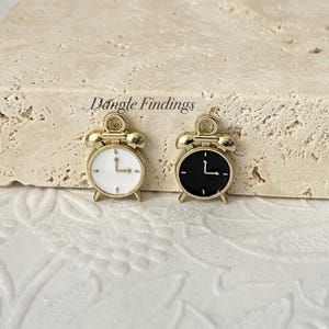 May include: Two gold-tone alarm clock charms, one with a white face and one with a black face.
