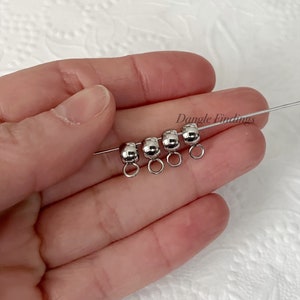 May include: Four silver-toned metal bead caps with jump rings. The bead caps are round and have a smooth finish. The jump rings are attached to the bead caps and are open.