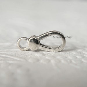 May include: Silver-toned metal clasp with a loop on one end and a spring-loaded clasp on the other. Dangle Findings is printed on the clasp.