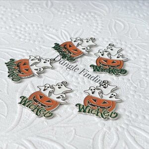 Pode incluir: Cinco pingentes de prata com uma ab&oacute;bora com fantasmas dentro. Cada pingente tem a palavra "Wicked" escrita em letras verdes.
