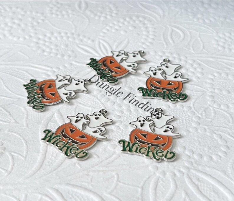 Pode incluir: Cinco pingentes de prata com uma ab&oacute;bora com fantasmas dentro. Cada pingente tem a palavra "Wicked" escrita em letras verdes.