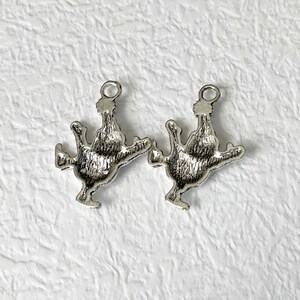 May include: Two silver charm pendants in the shape of a rooster, each with a loop at the top for attaching to a chain or bracelet.