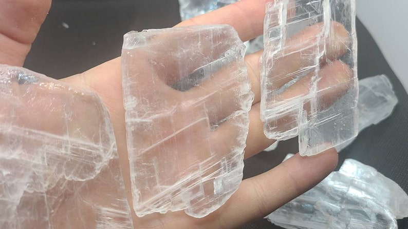 May include: A collection of clear selenite crystal slabs with a layered, striated texture. The crystals are translucent and have a natural, raw appearance.