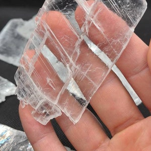 May include: A cluster of clear selenite crystals with a layered, striated texture. The crystals are arranged in a fan shape and have a translucent appearance.