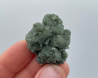 Puede incluir: Un cúmulo de formaciones cristalinas verdes. Los cristales están agrupados en una forma natural y tosca.