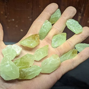 May include: A collection of green and yellow crystal stones of various sizes and shapes. The stones are translucent and have a natural, rough texture.