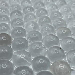 May include: A close-up view of a large quantity of clear glass beads with a small, etched circle on each bead.