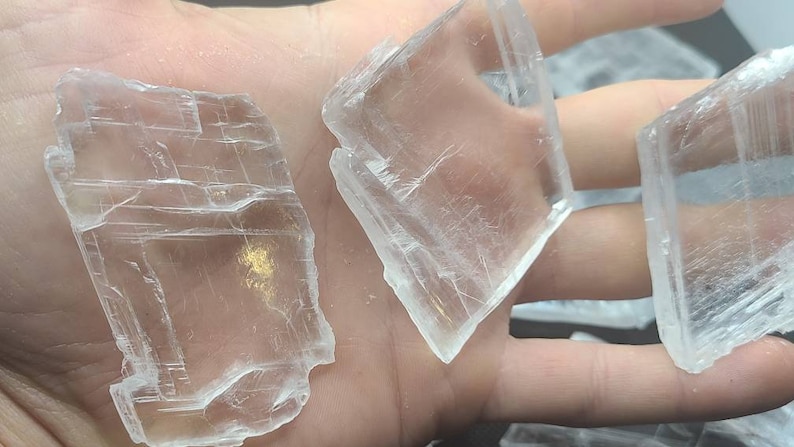 May include: Three clear, translucent selenite crystals with a layered, striated texture. The crystals are various sizes and shapes, with one being rectangular and two being more irregular.