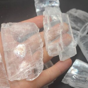 May include: A collection of clear, translucent selenite crystal pieces with a layered, striated texture. The crystals are various sizes and shapes, with some having a slightly iridescent sheen.