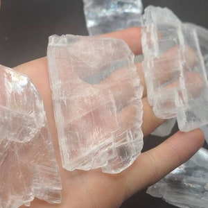 May include: A collection of clear selenite crystal slabs with a layered, striated texture. The crystals are translucent and have a slight shimmer.