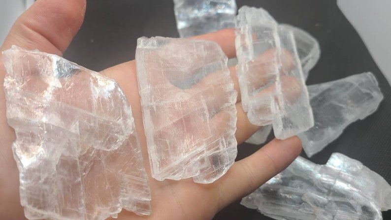 May include: A collection of clear selenite crystal slabs with a layered, striated texture. The crystals are translucent and have a slight shimmer.