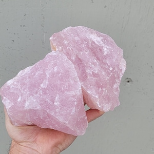 May include: Two large, raw, pink rose quartz crystals. The crystals are rough and have a natural, unpolished look.
