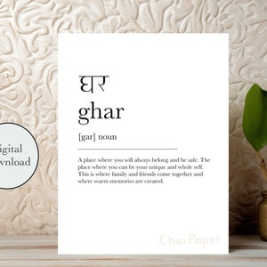 May include: A white print featuring the Hindi word "ghar" and its English translation, "ghar", with a definition. The print is on a wooden surface with a textured background and a small gold vase with green leaves.