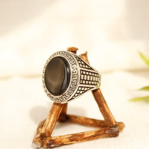 May include: A silver ring with a black oval stone set in a geometric design. The ring is displayed on a wooden ring holder.